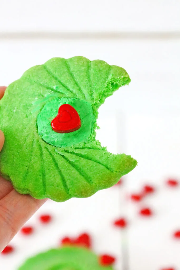 hand holding grinch thumbprint cookie with bite taken out of it
